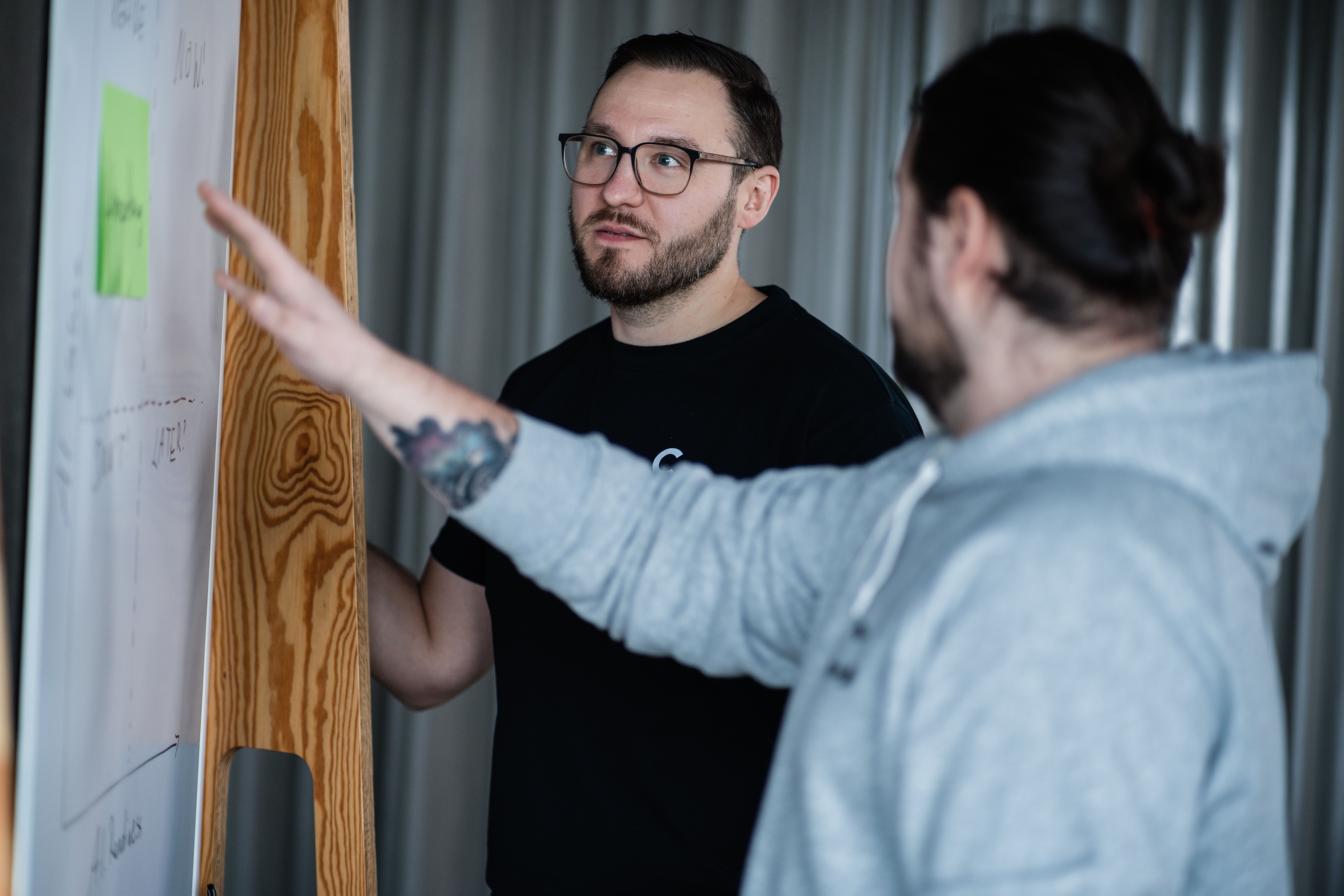 Zwei Männer stehen am Flipchart, einer zeigt mit ausgestrecktem Arm auf das Diagramm und erklärt es